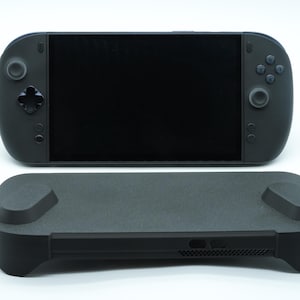 May include: A black handheld gaming console with a large rectangular screen, a directional pad, two analogue sticks, and four action buttons, accompanied by a separate black protective case with a textured surface and two raised thumbstick covers.