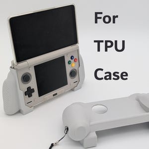 May include: A light gray TPU case for a handheld gaming console, shown both installed on the device and as a separate unit. The console features a dual-screen design, black screens, and colorful action buttons. The text "For TPU Case" is visible.