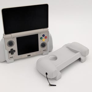 May include: A light grey handheld games console with a black screen and coloured buttons. A matching grey grip is next to the console. The console has a clamshell design and a directional pad.