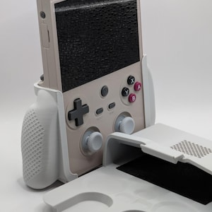 Puede incluir: Consola de juegos portátil en beige claro y gris. La pantalla es negra, los botones y la cruceta son grises. También se incluye un agarre y una funda grises a juego, para una configuración de juego completa.