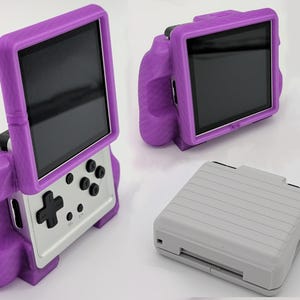 May include: A handheld gaming console featuring a silver body with black buttons and a directional pad, encased in a textured purple grip frame. The device is shown in an upright position and also folded closed as a compact, light grey rectangular unit.