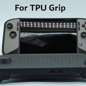 以下が含まれることがあります： タンカラーのフェイスプレートと黒いコントロールを備えた携帯型ゲーム機で、黒いTPUグリップカバーの後ろに配置されています。コンソールの上の黒い文字で「For TPU Grip」と印刷されています。コンソールには画面とボタンが付いています。