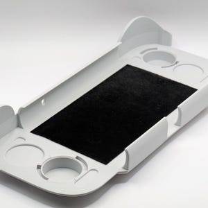 May include: A white plastic rectangular tray featuring a central black felt-lined rectangular insert. The tray includes raised side walls and four circular recessed cutouts positioned at the corners, designed to hold small cylindrical objects.