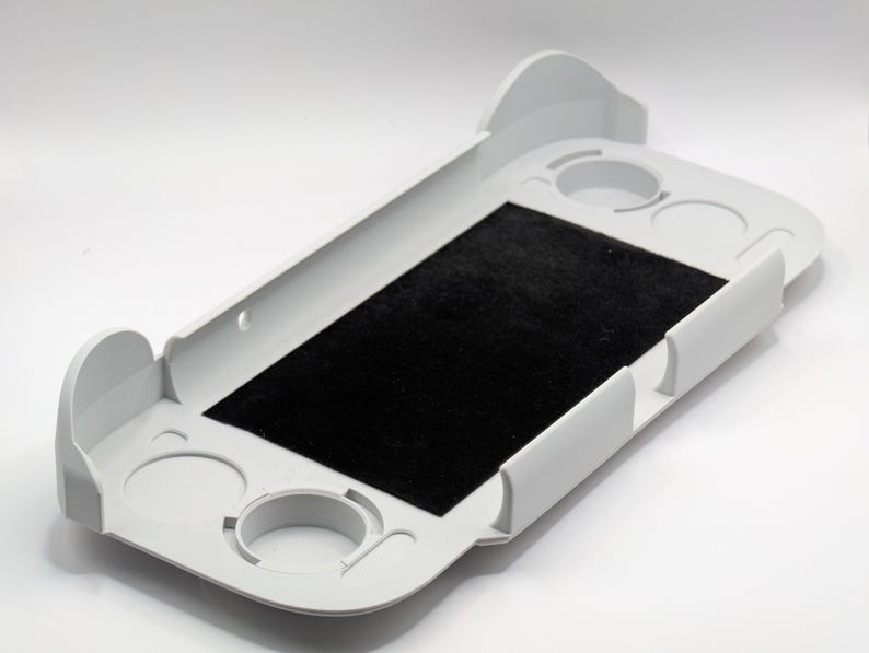May include: A white plastic rectangular tray featuring a central black felt-lined rectangular insert. The tray includes raised side walls and four circular recessed cutouts positioned at the corners, designed to hold small cylindrical objects.