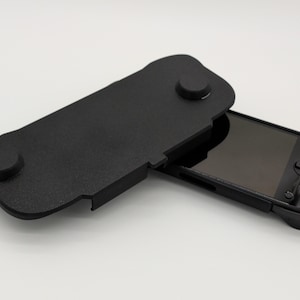 Pu&ograve; includere: Console di gioco portatile nera con custodia protettiva nera abbinata. La custodia &egrave; aperta, rivelando lo schermo e i comandi della console. La custodia ha due sporgenze circolari e una superficie strutturata.