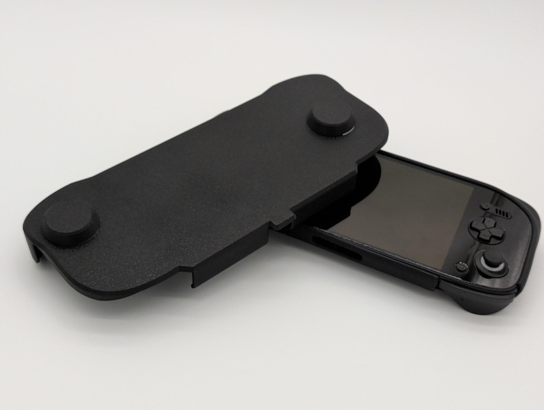 Pu&ograve; includere: Console di gioco portatile nera con custodia protettiva nera abbinata. La custodia &egrave; aperta, rivelando lo schermo e i comandi della console. La custodia ha due sporgenze circolari e una superficie strutturata.