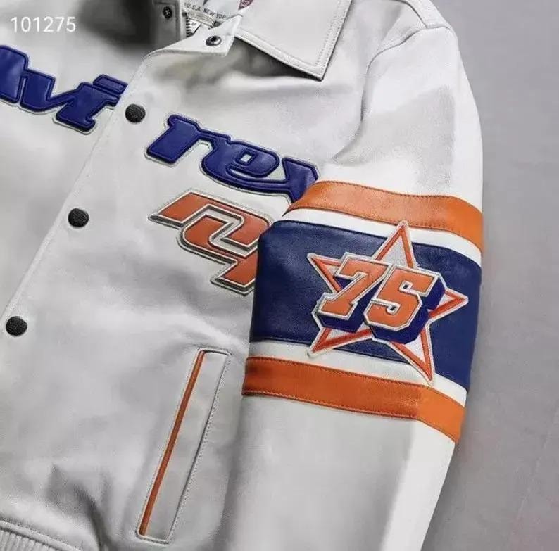 Puede incluir: Chaqueta de cuero blanca con detalles azules y naranjas. La manga muestra el n&uacute;mero "75" dentro de una estrella. La chaqueta tiene cuello y cierre de botones. La palabra "re" es visible en azul.