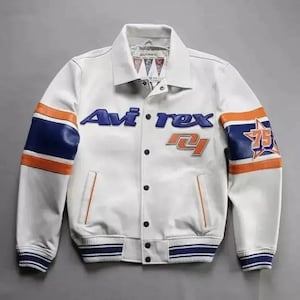 Puede incluir: Chaqueta de cuero blanca con detalles azules y naranjas. La chaqueta presenta el texto "Avi'rex" en azul, junto con el n&uacute;mero "75" en la manga derecha. Tiene cierre de botones y cuello.