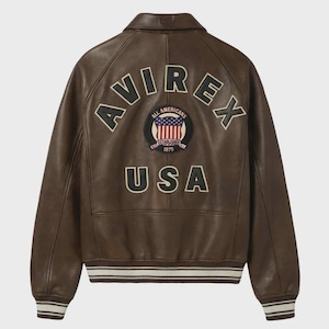 May include: Brown leather jacket with the word "AVIREX" arched across the back in black and cream lettering. Below the lettering is a circular patch with the words "ALL AMERICANS ESTABLISHED 1975" and a USA flag design. The word "USA" is below the patch.