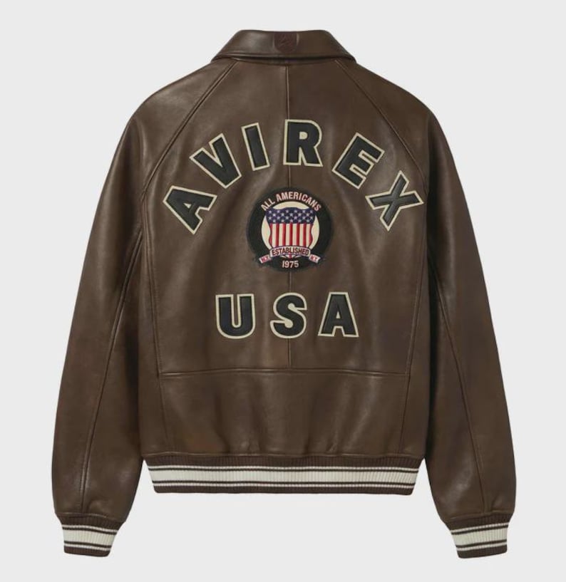 May include: Brown leather jacket with the word "AVIREX" arched across the back in black and cream lettering. Below the lettering is a circular patch with the words "ALL AMERICANS ESTABLISHED 1975" and a USA flag design. The word "USA" is below the patch.