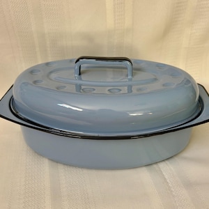 May include: A light blue enamel roasting pan with a matching lid. The oval-shaped pan has a black rim and handle. The lid has a handle and several small holes. The pan is designed for cooking.