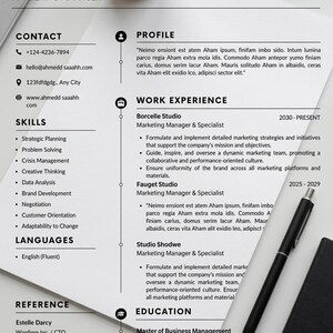 May include: A resume for AHMDD SAAH, a Marketing Manager, with contact information, skills, work experience, and education. A black pen and a small black notebook are on the white surface. A small potted plant is in the upper left corner.