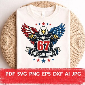May include: White t-shirt featuring a graphic of an eagle riding a motorcycle with wings in red, white, and blue. The design includes the number "67" and the text "AMERICAN RIDERS". Stars in red, white, and blue are also present.