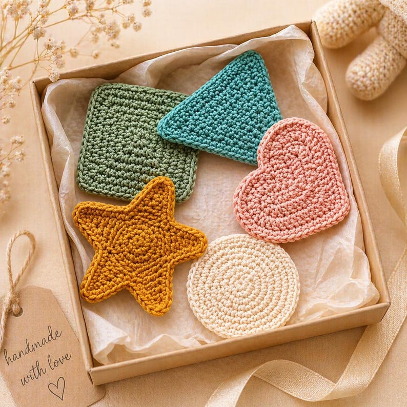 May include: A box of handmade crochet items in various shapes and colors. Includes a green square, a teal triangle, a pink heart, a yellow starfish, and a cream-colored circle. The box also contains a tag that says "handmade with love".