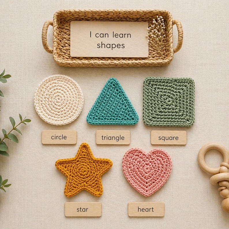 May include: A collection of crocheted shapes, including a circle, triangle, square, star, and heart, in various colors. Each shape is labeled with its name on a wooden tag. A woven basket with the text "I can learn shapes" is at the top.