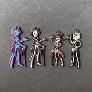 May include: Four enamel pins featuring skeleton figures in various outfits. One is purple with a fox-like head, another is a pirate, a third wears a top hat, and the last has a TV head. Each pin has a cane and a metallic finish.