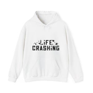 May include: White hoodie with a front pocket and drawstring. The black text "LIFE CRASHING" is printed across the chest in a pixelated font. The hoodie has a hood and is made of a soft material.