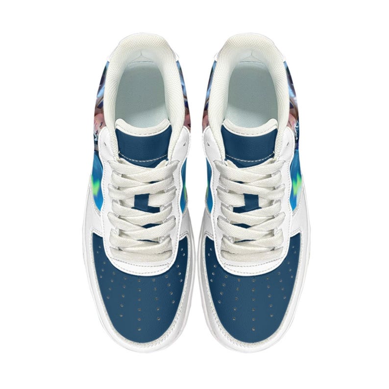 Op de afbeelding: Paar wit en blauwe sneakers met een laag model. De sneakers hebben een witte basis met blauwe accenten op de neus en hiel. Het ontwerp bevat een kleurrijke afbeelding aan de zijkant en bovenkant, met witte veters.