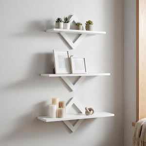 Puede incluir: Tres estantes flotantes blancos con un diseño geométrico están montados en una pared blanca. El estante superior contiene pequeñas plantas en macetas. El estante del medio muestra obras de arte enmarcadas. El estante inferior presenta velas y un nudo decorativo.