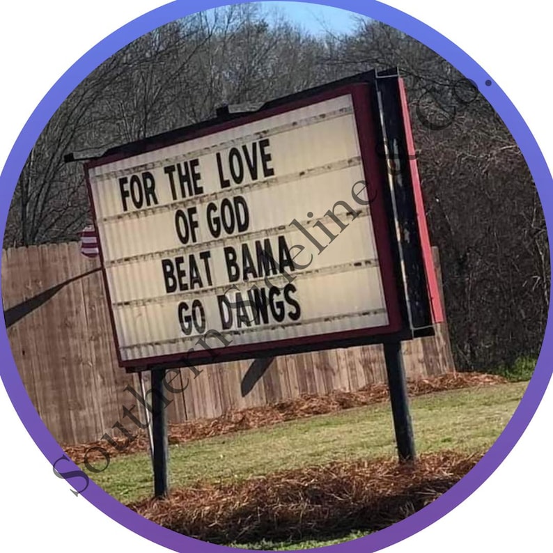 K&ouml;nnte beinhalten: Ein Stra&szlig;enschild mit der Aufschrift "FOR THE LOVE OF GOD BEAT BAMA GO DAWGS" in wei&szlig;en Buchstaben. Das Schild ist rot und schwarz umrandet, vor dem Hintergrund von B&auml;umen und einem Holzzaun.