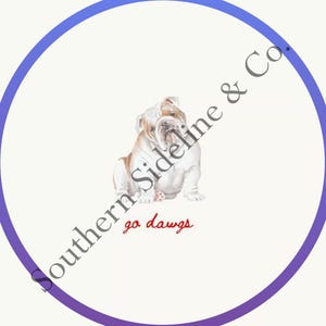 K&ouml;nnte beinhalten: Ein rundes Design mit einer Aquarellillustration einer Bulldogge. Die Bulldogge ist wei&szlig; und hellbraun, mit den Worten "go dawgs" in roter Schrift. Das Design wird von einem lila und blauen Kreis mit dem Text "Southern Sideline & Co." in grauer, geschwungener Schrift umrahmt.