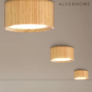 May include: Three wooden ceiling lights with a cylindrical design. The lights are made of light-colored wood and emit a warm, inviting glow. The brand name "ALVENHOME" is visible in the top right corner. These lights are suitable for home decor.