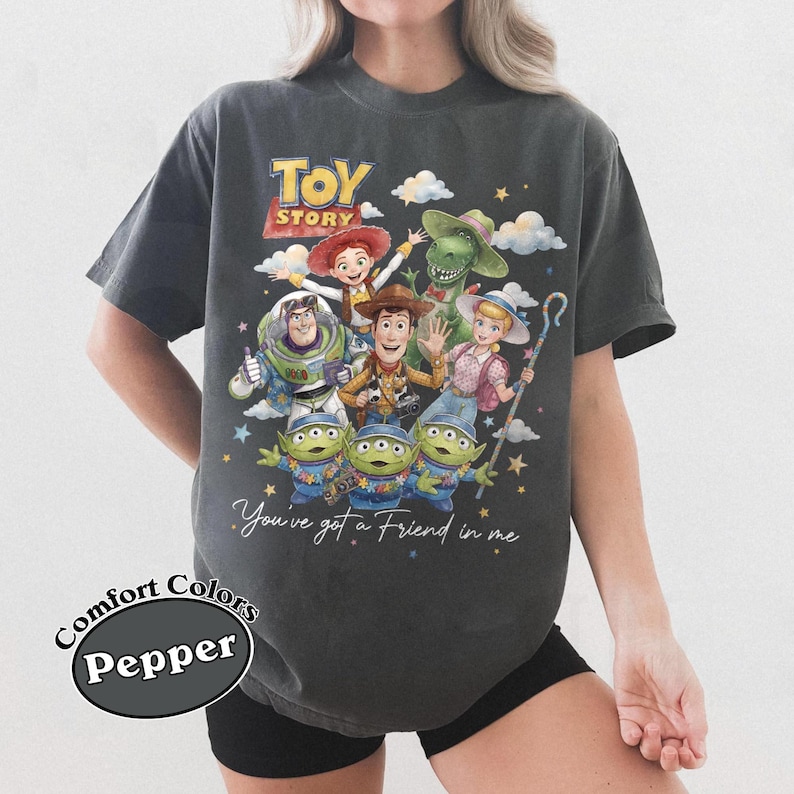 Pu&ograve; includere: T-shirt grigio scuro con una grafica colorata dei personaggi di Toy Story, tra cui Woody, Buzz Lightyear e i piccoli omini verdi. La maglietta presenta la scritta "You've got a Friend in me" e il logo Comfort Colors Pepper.