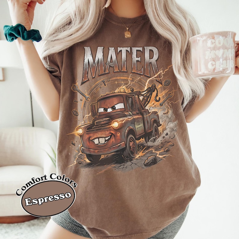 May include: Espresso-colored t-shirt featuring a graphic of Mater from the movie Cars. The design includes the word "MATER" in large, distressed lettering above the cartoon tow truck. The shirt also has the words "Comfort Colors" and "Espresso" printed on it.