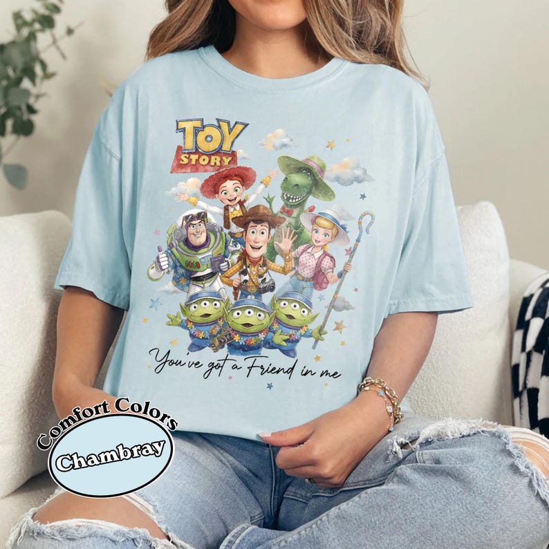 Pu&ograve; includere: T-shirt azzurra con una grafica di Toy Story con Woody, Buzz Lightyear e i piccoli omini verdi. Il testo "Toy Story" &egrave; in alto, con "You've got a Friend in me" sotto. La maglietta &egrave; etichettata "Comfort Colors Chambray".