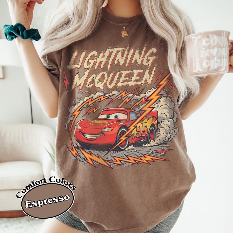 May include: Espresso-colored t-shirt featuring Lightning McQueen from the Cars movie. The graphic shows the red race car with the number 95, surrounded by lightning bolts and smoke. The shirt also has the words "Lightning McQueen" in a distressed font.