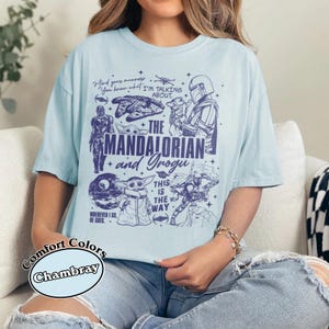 May include: Pale blue t-shirt with illustrations of characters from "The Mandalorian" series. The shirt features the text "The Mandalorian and Grogu" and other phrases. The shirt is a Comfort Colors Chambray.