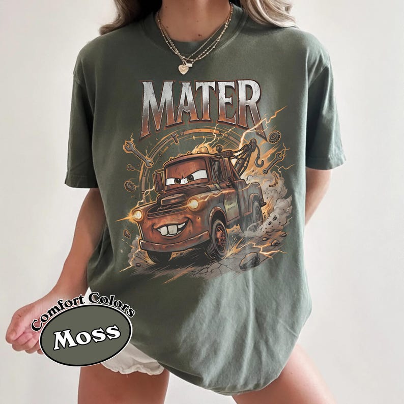 May include: Moss green t-shirt featuring a graphic of Mater from the movie Cars. The design includes the word "MATER" in a distressed font above the cartoon tow truck. The shirt is a Comfort Colors brand.