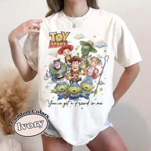 Pu&ograve; includere: T-shirt color avorio con una grafica colorata dei personaggi di Toy Story, tra cui Woody, Buzz Lightyear e i piccoli omini verdi. Il testo "You've got a Friend in me" &egrave; sotto. La maglietta &egrave; di Comfort Colors.