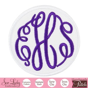 May include: A white, round, iron-on patch with a purple embroidered monogram of the letters "JLS". The patch is handmade and has a white border.