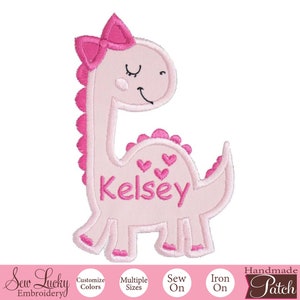 May include: Pink dinosaur-shaped iron-on patch with a pink bow and the name "Kelsey" embroidered in pink.