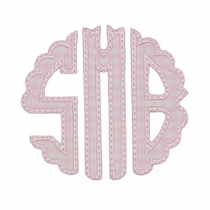 May include: A circular monogram featuring the letters S, M, and B in a scalloped font style. The letters are filled with a light pink and white gingham check pattern and are outlined with a decorative pink stitched border on a plain background.