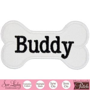 May include: White iron-on patch shaped like a bone with the name "Buddy" embroidered in black thread.
