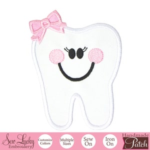 May include: White embroidered tooth with a pink bow, black eyes, and a smiling mouth. The tooth is a sew-on or iron-on patch.