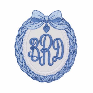 May include: An oval-shaped embroidered patch featuring a white center with the blue monogram letters BRD in a script font. The border is a braided blue pattern topped with a blue bow and a small blue heart charm hanging from the center.