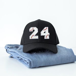 Baseball number patch applied to a black baseball cap showing numbers 2 and 4 with white varsity style jersey numbers and red baseball stitch embroidery. Custom iron on or sew on baseball number patches used for baseball uniforms, team jerseys, little league teams, travel ball players, and personalized sports apparel.