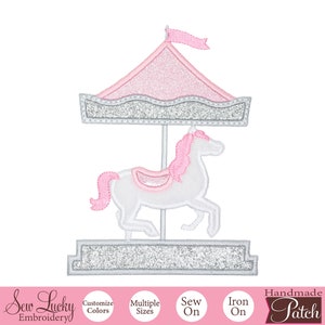 May include: A pink and silver glitter iron-on patch of a carousel horse. The horse is white with a pink mane and tail. The carousel has a pink canopy with a silver glitter base.