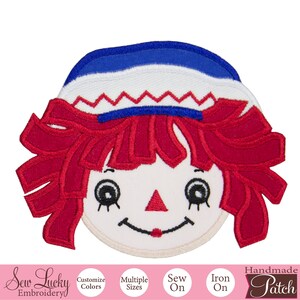 May include: Red, white, and blue embroidered iron-on patch of a rag doll with a smiling face.  The patch is handmade and says "Handmade Patch" at the bottom.