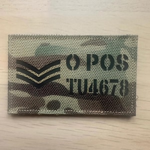Może przedstawiać: Prostokątna naszywka z kamuflażem. Naszywka posiada trzy czarne szewrony i czarny napis "OPOS TU4678". Naszywka jest prawdopodobnie wykonana z wytrzymałej tkaniny.