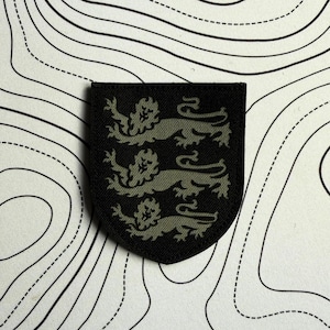 May include: A black patch featuring three olive green lions in a heraldic design. The patch is shield-shaped and set against a white background with a black topographic map pattern.