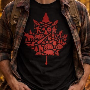 May include: A black short-sleeved t-shirt featuring a large red graphic in the shape of a maple leaf. The graphic is composed of various small icons including a bear, a moose, an igloo, a pine tree, a canoe paddle, and outdoor activity silhouettes.