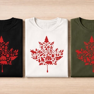May include: Three t-shirts in black, white, and olive green, each featuring a large red maple leaf graphic composed of various outdoor-themed icons including a bear, an igloo, a canoe, a pine tree, and a paddle extending from the bottom.