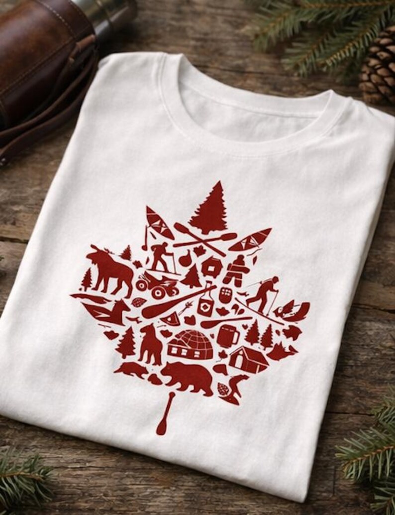 May include: A white short-sleeved t-shirt featuring a large red graphic in the shape of a maple leaf. The leaf is composed of various small silhouettes including a moose, bear, igloo, pine trees, canoe, paddles, and outdoor activity icons.