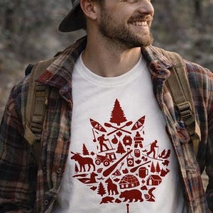 Peut inclure: T-shirt blanc avec un motif de feuille d'érable rouge rempli d'illustrations sur le thème du plein air. Le t-shirt est porté par une personne portant une chemise à carreaux et une casquette. Le motif comprend des images de canoës, d'arbres et d'animaux sauvages.
