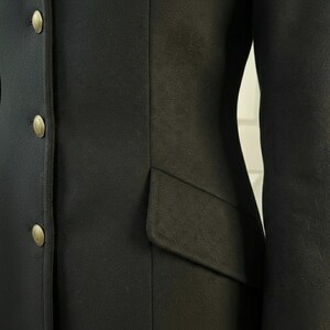 K&ouml;nnte beinhalten: Nahaufnahme eines schwarzen Blazers mit drei goldenen Kn&ouml;pfen auf der linken Seite. Der Blazer hat eine taillierte Passform und eine Tasche auf der rechten Seite. Der Stoff scheint ein glattes, gewebtes Material zu sein.