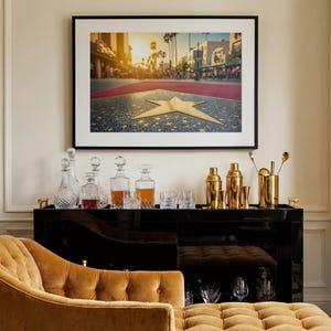 May include: A framed photograph of the Hollywood Walk of Fame with a gold star. Below the photograph is a black bar cart with decanters, glassware, and gold bar tools. A gold chaise lounge is in the foreground.